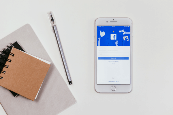 Facebook on a mobile phone with pad of paper and pen to one side